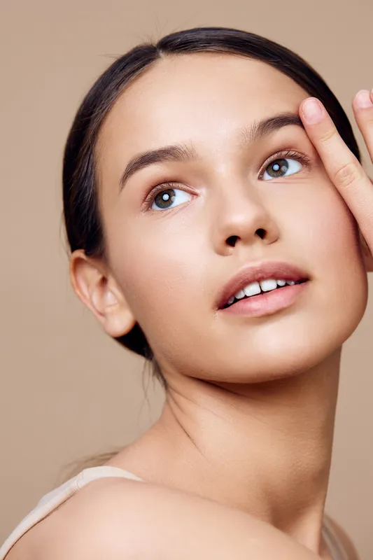 Elegant portrait of a young woman with clear skin, showcasing natural beauty and a serene expression against a soft beige background
