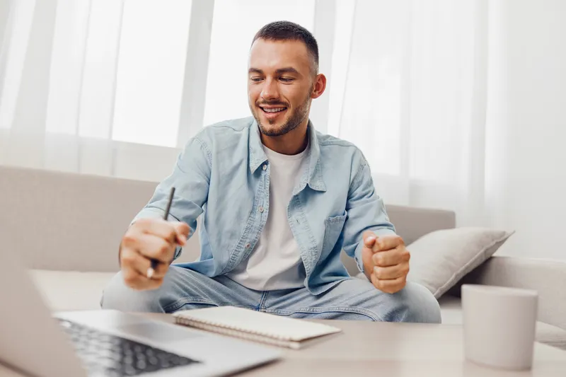 Smiling man engaged in video call, wearing casual attire, sitting comfortably at home. Embracing modern remote work culture and vibrant lifestyles.