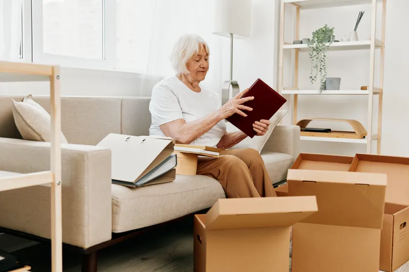 Пожилая женщина сидит на диване дома среди коробок