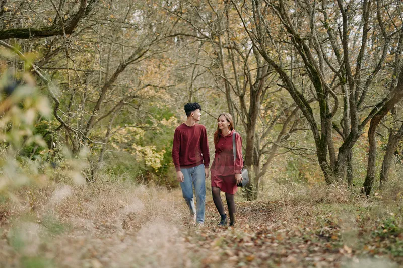 An authentic, candid scene shows a couple strolling through a sunlit autumn forest, wearing casual fall apparel, capturing a genuine connection amid golden leaves and quiet, natural beauty.