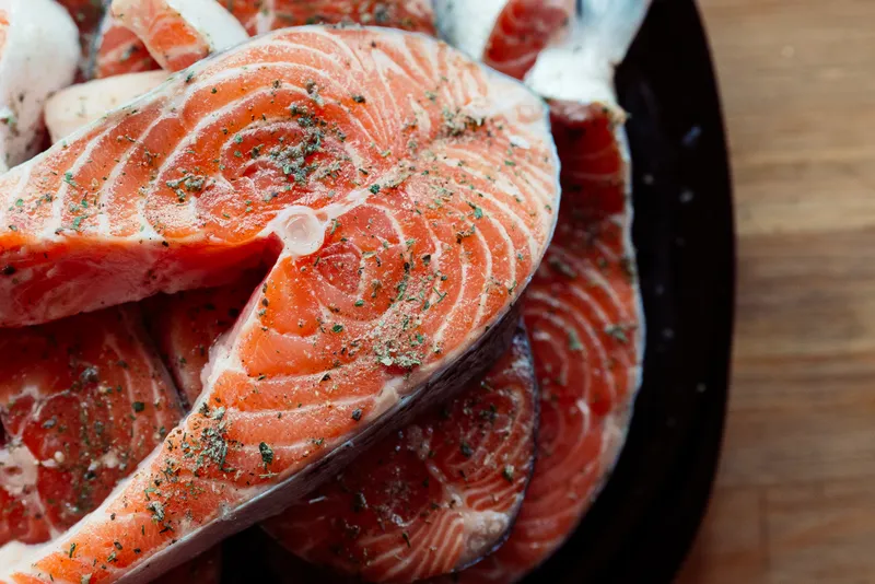 Нарезанная красная рыба на тарелке, приготовление морепродуктов на деревянном фоне