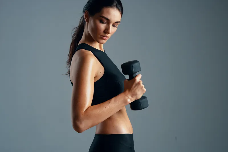 Спортивная женщина напрягает мышцы, демонстрируя стройную фигуру и мотивацию к тренировкам