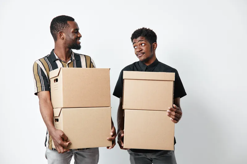 Two african american men with dark skin holding cardboard boxes for moving or delivery. Casual clothing, teamwork and cooperation in logistics or relocation activity.