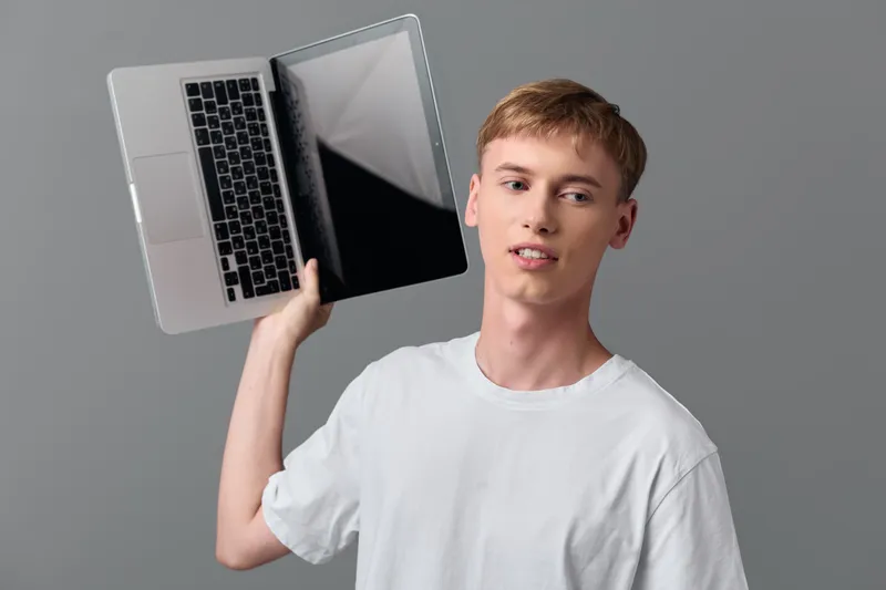 Male wearing a white tshirt holds an open laptop in a studio setup, illustrating modern technology and casual work style, a digital device used for online tasks and learning