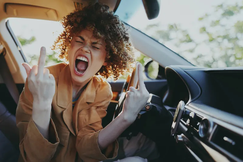 Candid woman in a car, shouting with joy, sunlit interior, casual outfit, celebratory moment captured in warm retro color and natural light