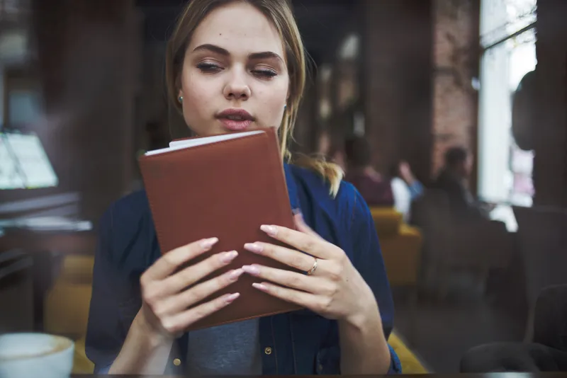 Деловая женщина с книгой в руках и чашкой кофе в кафе, ведущая активный образ жизни