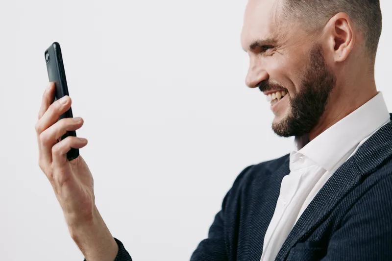 Professional man on a colored background, exuding confidence and focus, smiling softly at a phone, conveying emotion, ambition, and success in a modern business scene.