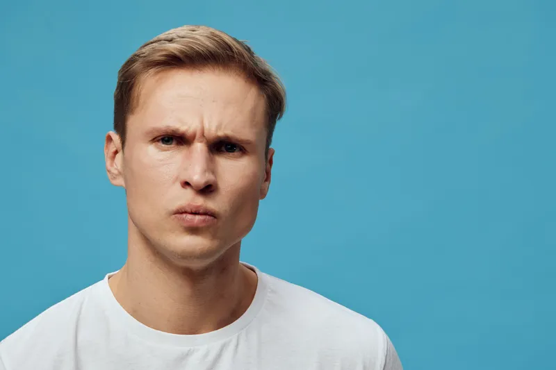 serious young man with thoughtful face white t-shirt blue background close-up mental health focus emotion expression concept