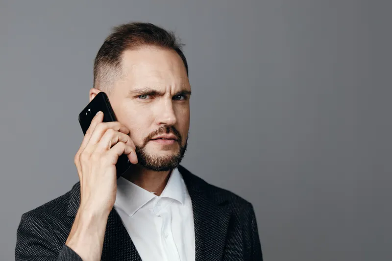 A professional man on a business call stands against a solid colored background, exuding focus, confidence, and determination through his poised posture.