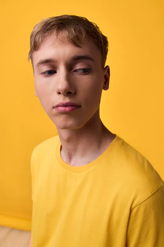 Young man in a yellow t-shirt against a matching yellow backdrop, casual fashion style, soft studio lighting, minimal composition, mood of calm and focus, versatile stock image.