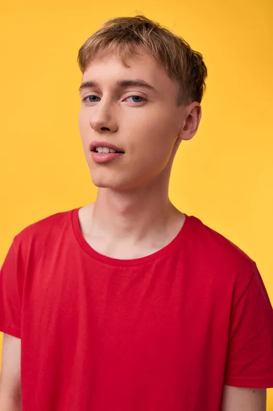 Young man wearing a red t-shirt stands against a bright yellow backdrop, casual style and confident expression, studio lighting highlighting clean lines and modern fashion vibe.