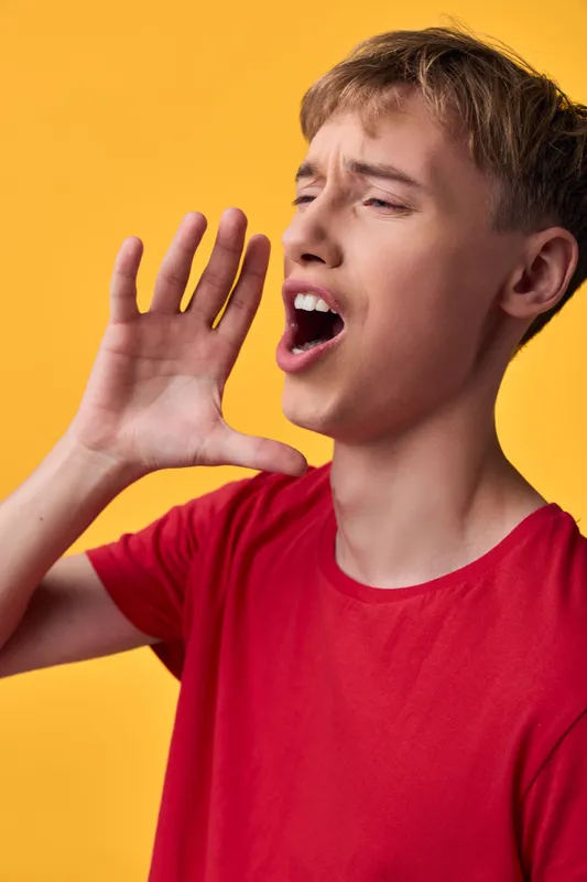 Shouting boy with hand cupped beside his mouth against a bright yellow backdrop, conveying loud voice and energetic expression, a dynamic youthful moment of action.