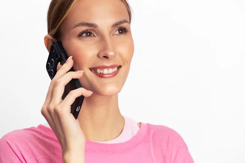 Smiling woman in pink sweater talking on smartphone. Close-up on white background. Concept for communication, technology, happiness, and positive emotions in everyday life.