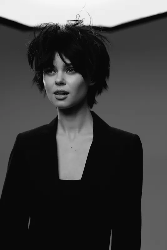 Black and white portrait of a young woman with short hair wearing a dark blazer and expressive look in studio background