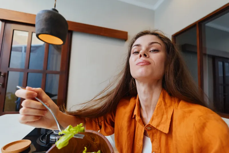 Уверенная в себе молодая женщина наслаждается вкусным салатом в хорошо освещённой современной кухне