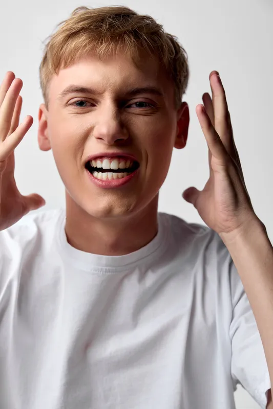 Energetic shouting expression and emotion from a youthful man in a white t shirt, captured in a dynamic studio closeup with raised hands, intense focus, a moment of excitement, bold composition with