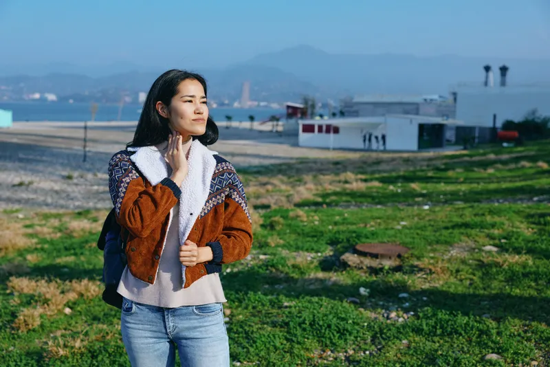 Woman outdoors fashion jacket coastal scenery calm confident pose, standing along the coast and enjoying sea breeze under natural light with a stylish casual mood
