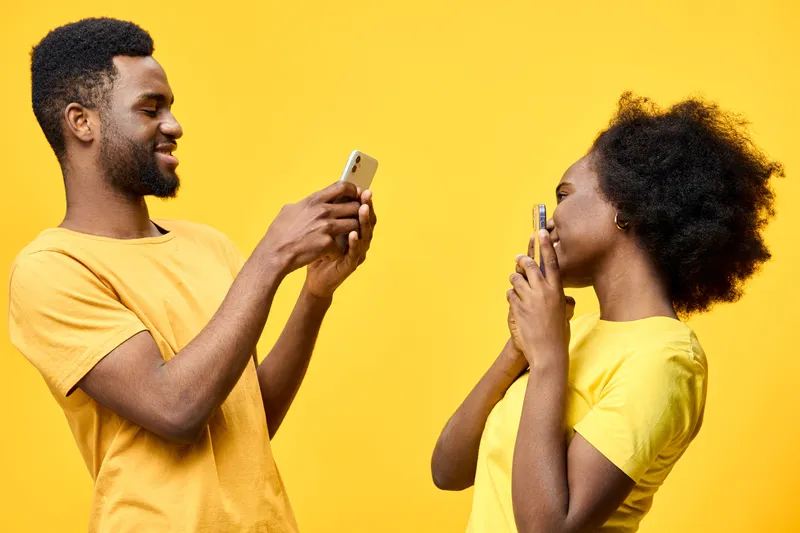 Smiling African couple taking selfies together against a vibrant yellow background, expressing joy and connection in matching yellow outfits