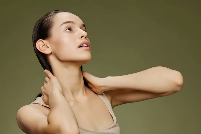 Young woman with a graceful pose, displaying confidence and elegance against a soft green background, wearing minimalistic clothing and showcasing healthy skin and hair