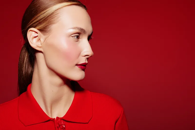 Profile of a young woman with clear skin and red lipstick wearing a red top against a red background. Concept of beauty, fashion, and minimalistic style.