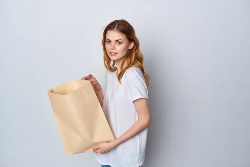 Женщина в белой футболке с пакетом продуктов, упаковкой, занимается покупками