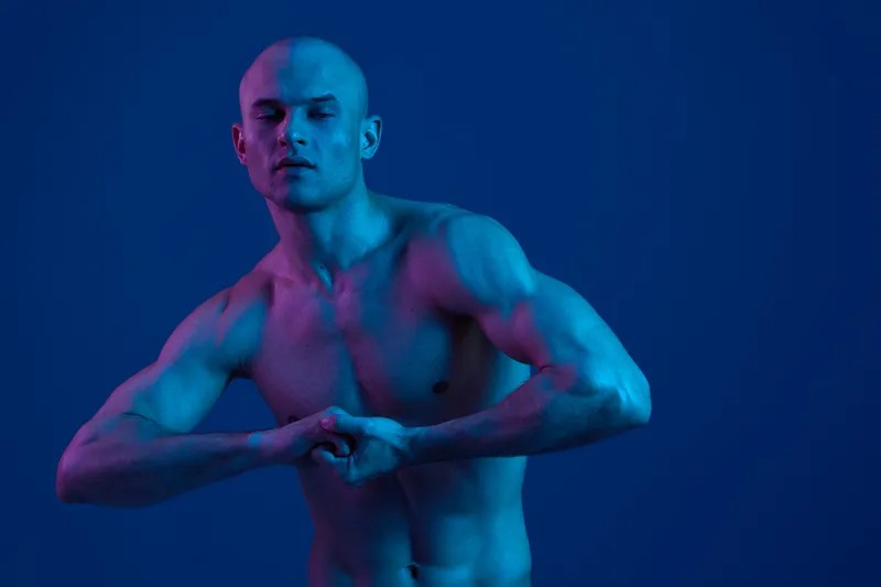 Strong man posing in a vibrant blue hue, showcasing his muscular physique with an elegant arm posture. The image is visually striking and captivating.
