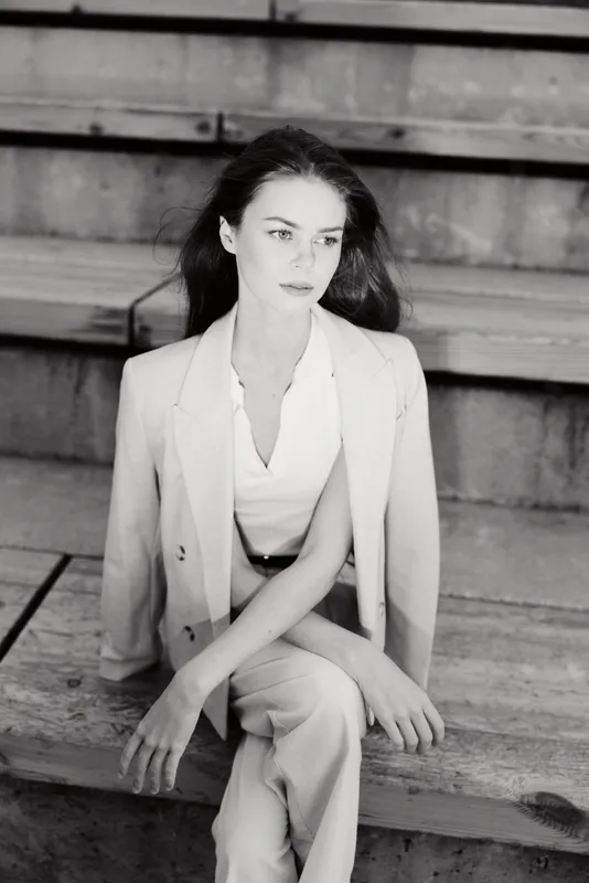 Black and white portrait of a thoughtful woman wearing light business suit sitting on wooden stairs with serious emotion urban background business concept