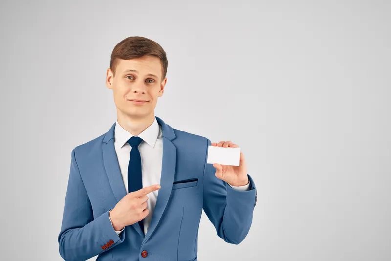 Деловой мужчина в костюме держит визитную карточку, предусмотрено место для рекламного текста