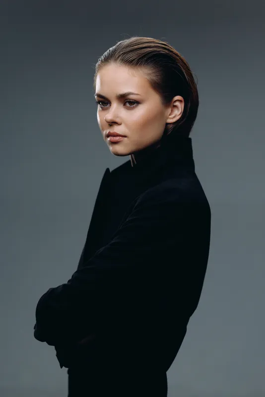 Serious young woman with short hair wearing black coat against gray background in studio.