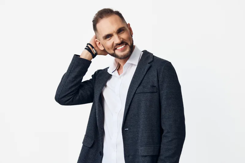 A confident business professional man stands with a relaxed smile against an isolated color background, exuding approachable charm, modern style, and readiness for corporate challenges in a polished