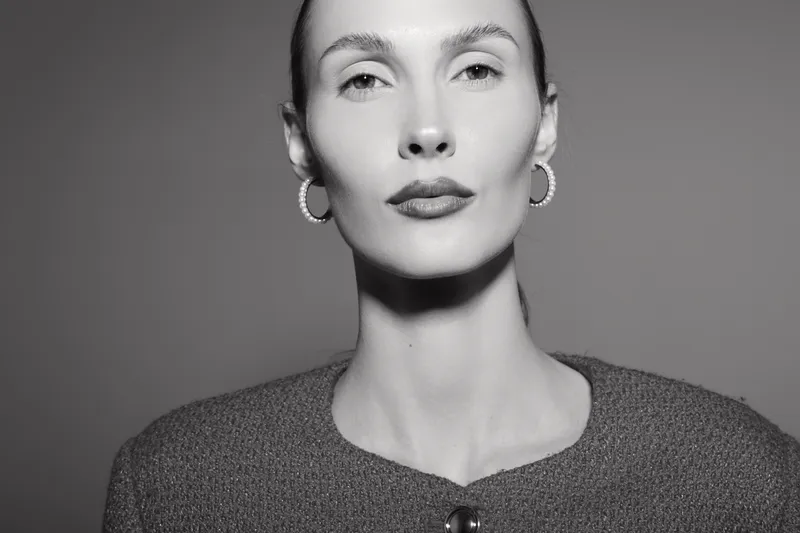 Elegant Caucasian woman with fair skin and hoop earrings poses confidently in a textured sweater against a plain background. Concept for style and beauty.