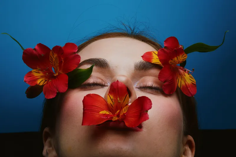 A serene portrait of a woman adorned with vibrant red flowers, conveying emotions of tranquility and beauty against a blue background