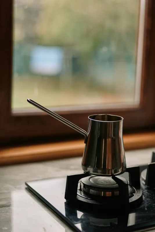 Close up of a moka pot on a stovetop brewing coffee, metal surface gleaming under warm light, a quiet kitchen scene capturing a daily espresso ritual