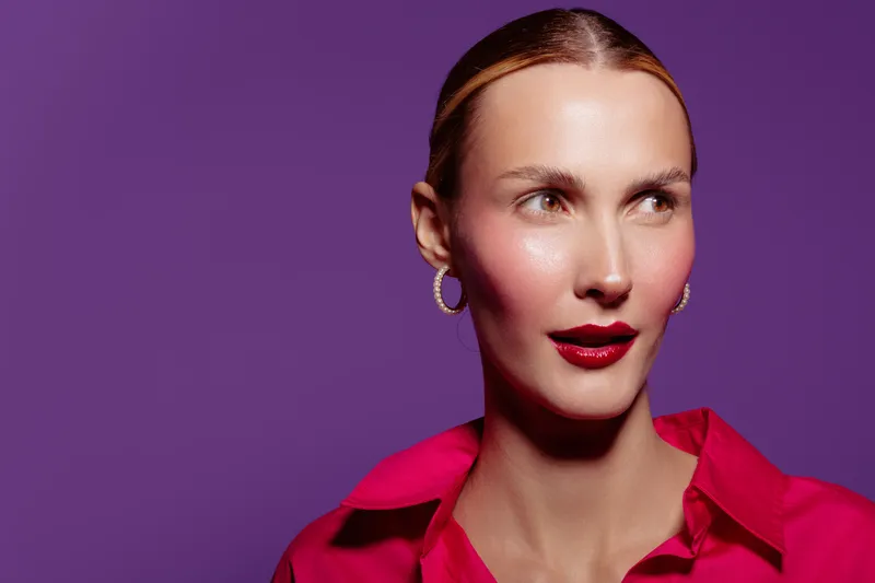 Portrait of a confident woman with red lipstick and hoop earrings wearing a red shirt against a purple background. Concept of fashion, beauty, and modern style with vibrant colors.