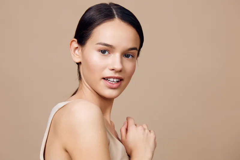 Portrait of a young woman with a natural makeup look, exhibiting confidence and serenity against a neutral beige background, ideal for beauty and skincare concepts