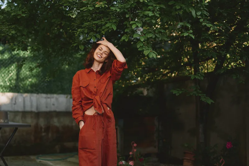 Happy woman in red outfit enjoys sunny outdoor moment, casual lifestyle portrait with greenery and relaxed smile, natural light and garden ambience