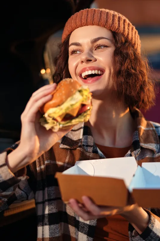 Woman burger smile takeout outdoor candid scene of a young woman laughing while eating a burger at golden hour glow, authenticity and mindful living captured with emotional storytelling.