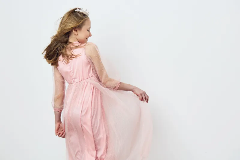 Young girl in a pink dress with a flowing skirt, enjoying a carefree moment, showcasing joy and innocence against a light background