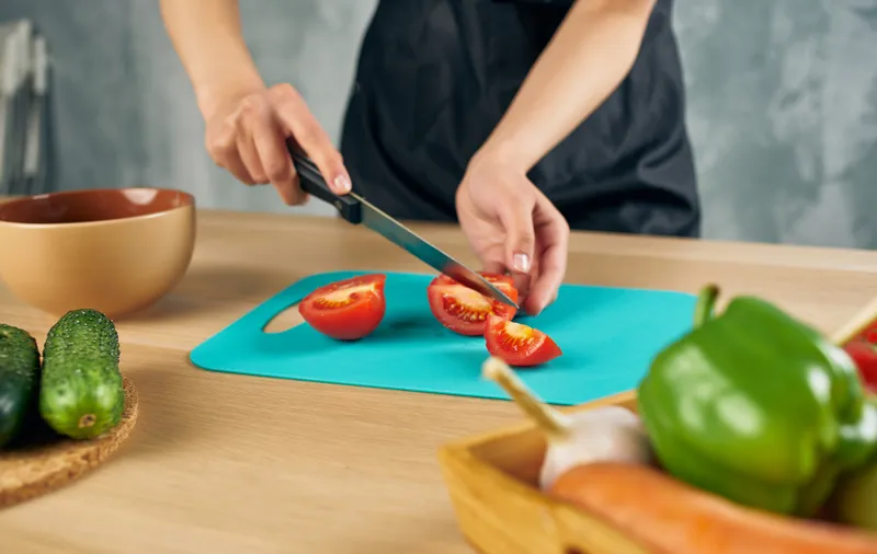 Женщина в черном фартуке нарезает овощи на кухне, готовит свежую еду
