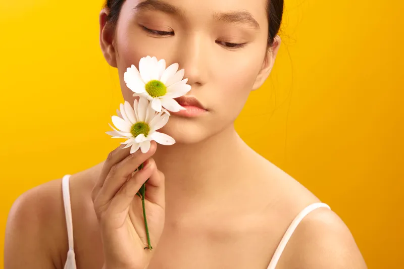 asian woman portrait closeup with white daisies near the lips, soft yellow background, calm mood, graceful elegance, delicate beauty, serene atmosphere and natural light.