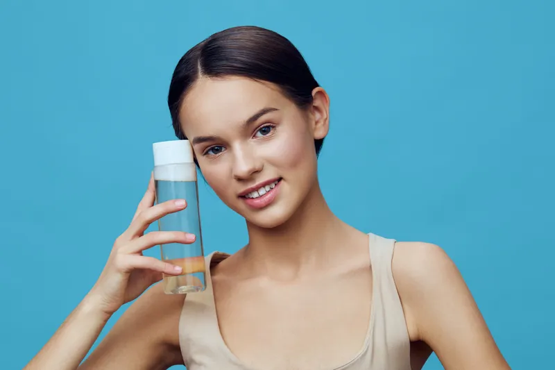 Young woman with a beauty drink, smiling happily against a bright blue background, promoting healthy lifestyle and wellness
