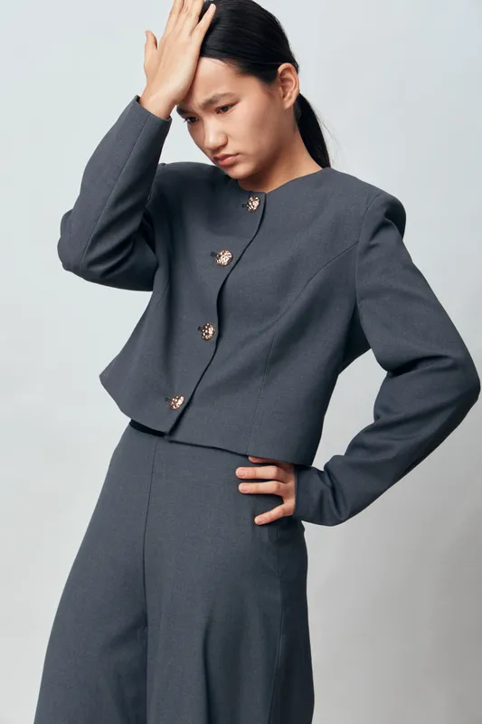 Woman in gray suit posing with hand on forehead and other on hip, serious expression, studio background, modern fashion outfit, elegant style and minimalistic look.