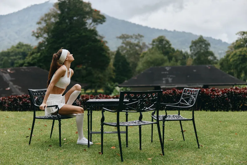 Young woman sitting on a chair in a beautiful outdoor setting, wearing stylish activewear, showcasing a relaxed and contemplative mood amidst green nature