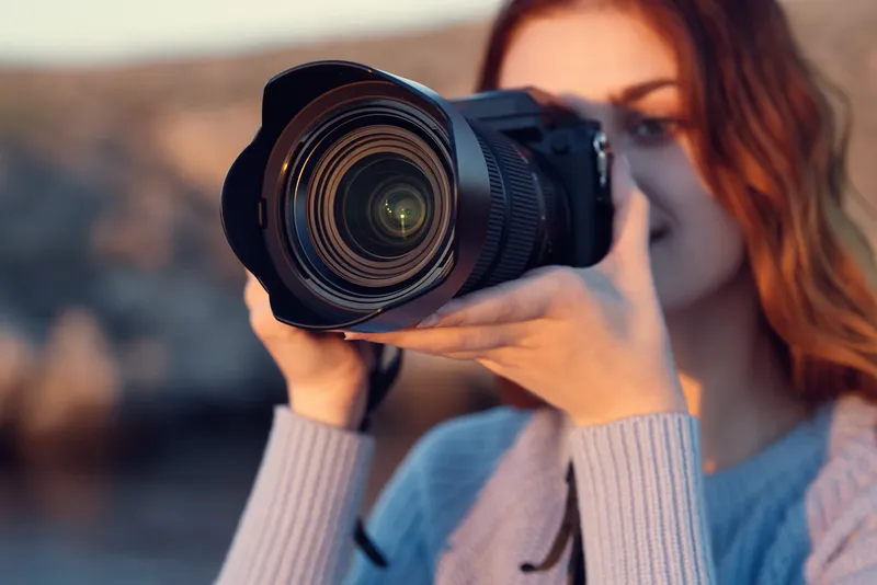 Симпатичная женщина с фотоаппаратом на природе в горах, на заднем плане река