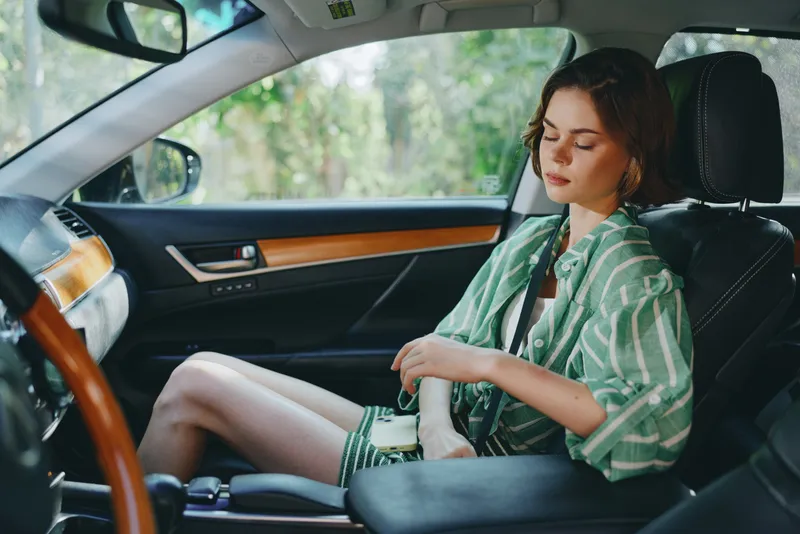 Woman seated in a car, wearing a green striped shirt, relaxed, with seatbelt fastened, front passenger position.