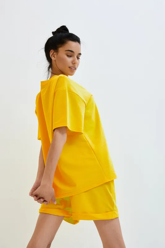 young woman in yellow casual outfit posing confidently against plain white background, showcasing modern streetwear style and relaxed natural pose