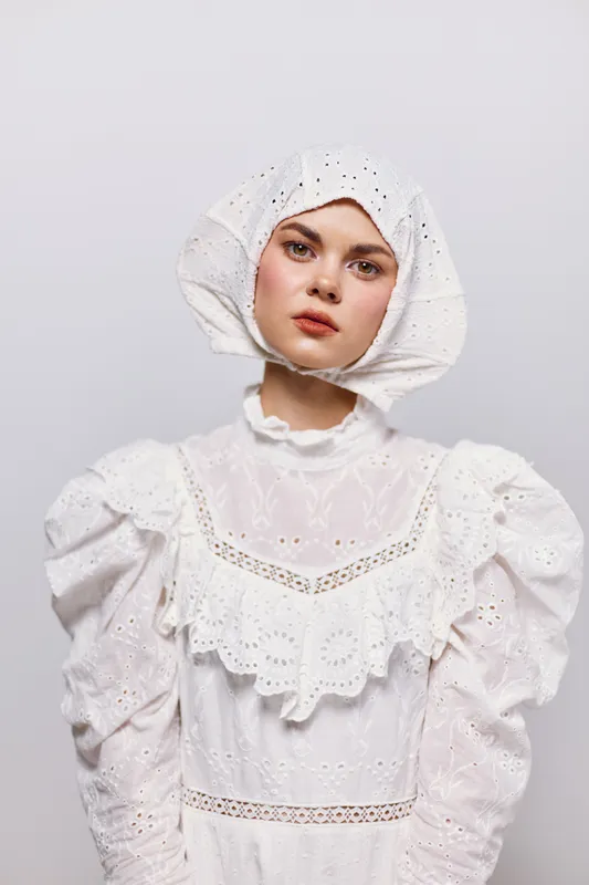 Young woman in a white vintage dress with puffed sleeves, showcasing an expressive face against a neutral background, reflecting elegance and nostalgia