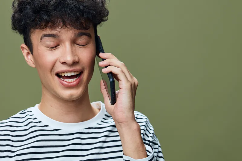 smiling man talking on phone with eyes closed wearing striped shirt, expressing joy and relaxation against green background, casual lifestyle emotion