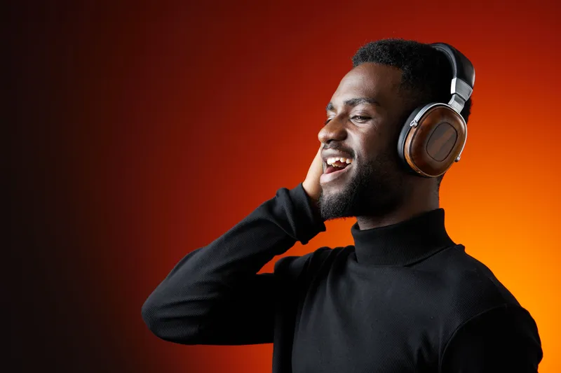 Happy young Black man listening to music with headphones, enjoying the rhythm and expressing joy in a vibrant orange background