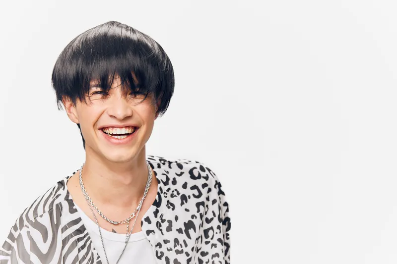 smiling man with black hair wearing patterned shirt and chain necklaces expressing happiness and joy isolated on a white background, stylish casual look